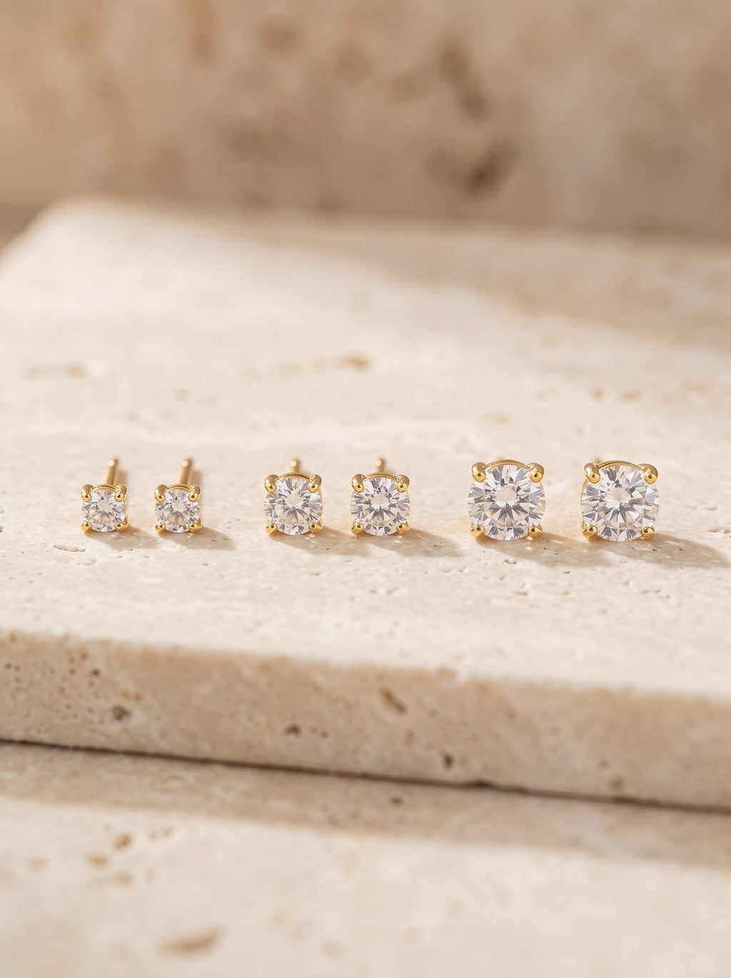 Three pairs of gold vermeil cubic zirconia stud earrings in a row on cream travertine