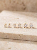 Three pairs of gold vermeil cubic zirconia stud earrings in a row on cream travertine