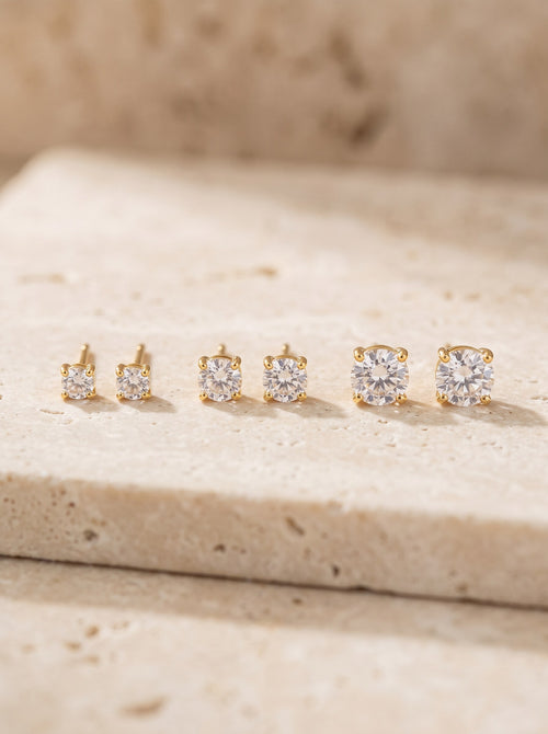 Three pairs of gold vermeil cubic zirconia stud earrings in a row on cream travertine