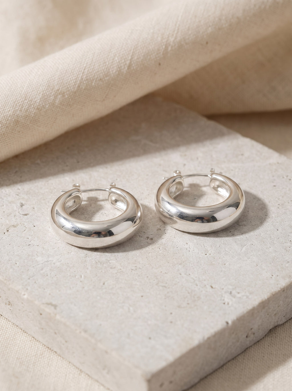 Pair of Dome Hoop Earrings in polished sterling silver on pale limestone