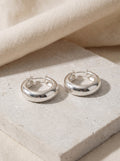 Pair of Dome Hoop Earrings in polished sterling silver on pale limestone
