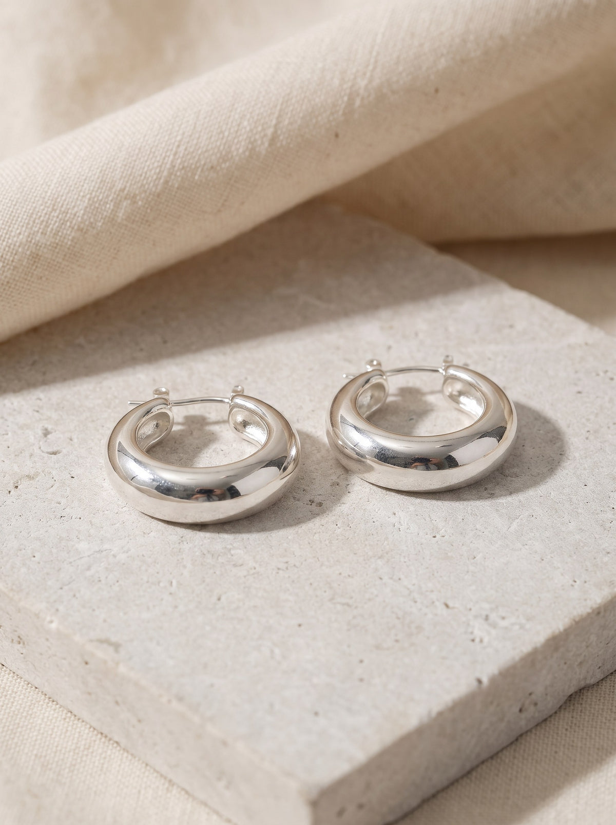 Pair of Dome Hoop Earrings in polished sterling silver on pale limestone