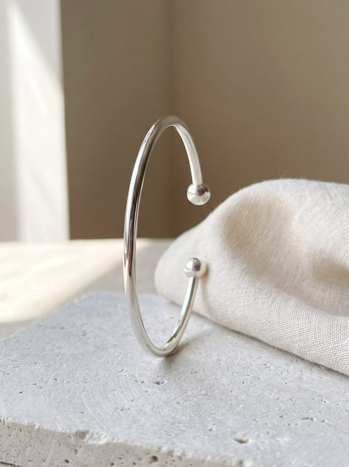 Fine Open Cuff Bangle in sterling silver standing on pale limestone