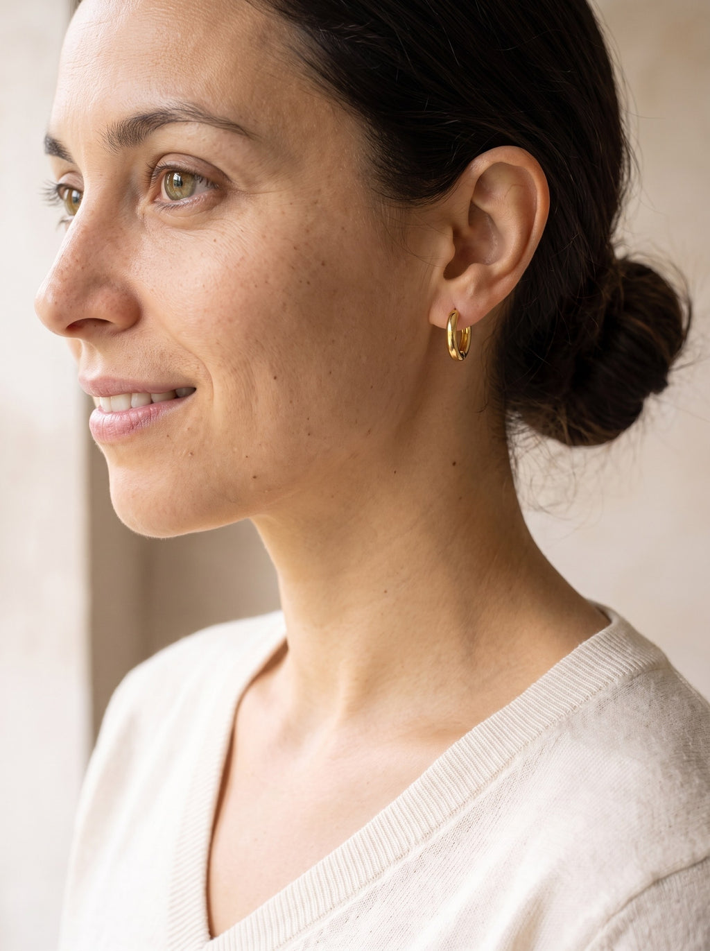 Woman wearing the gold Mini Huggie Hoop Earrings with her hair in a low bun