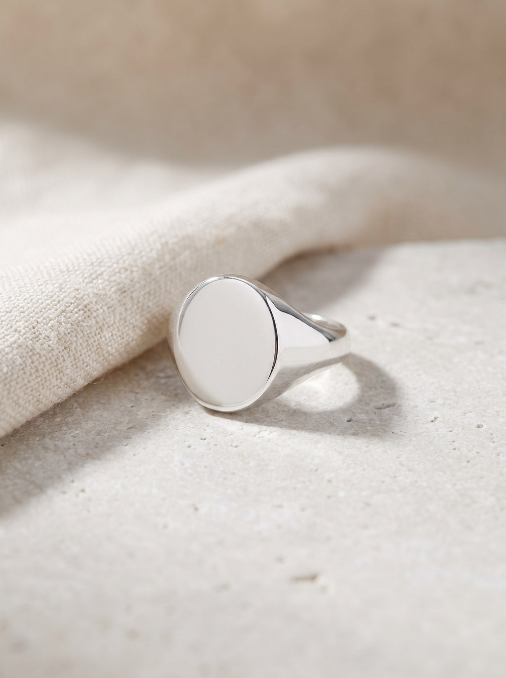 Oval Signet Ring in polished sterling silver lying on pale limestone beside cream linen