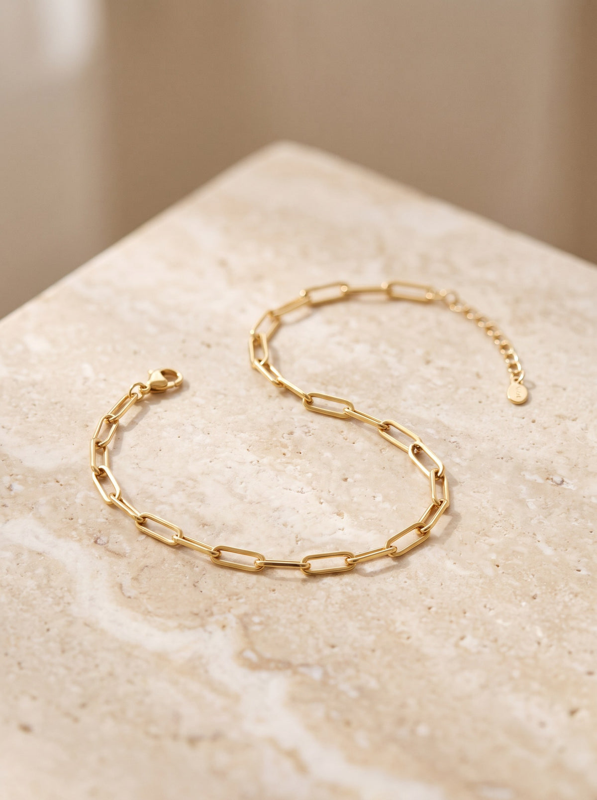 Paperclip Chain Bracelet in gold vermeil laid in a curve on cream travertine