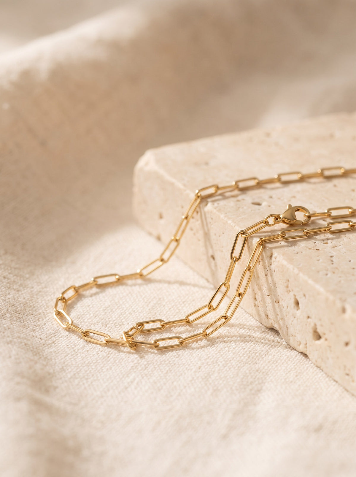 Paperclip Chain Necklace in gold vermeil draped over cream travertine stone