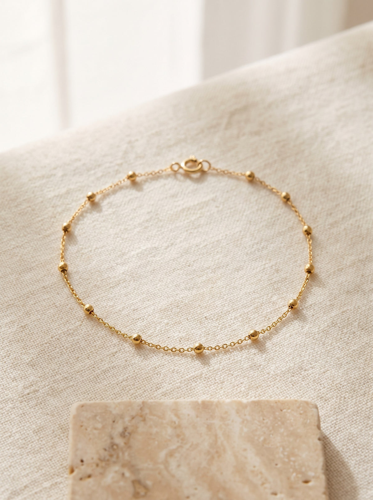Satellite Chain Bracelet in gold vermeil laid in a circle on cream linen